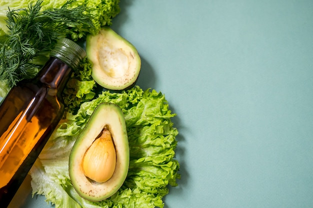 Green vegetables with glass boutle of oil on a green background Avocado Romano salad greens Top view No plastic Healthy diet concept