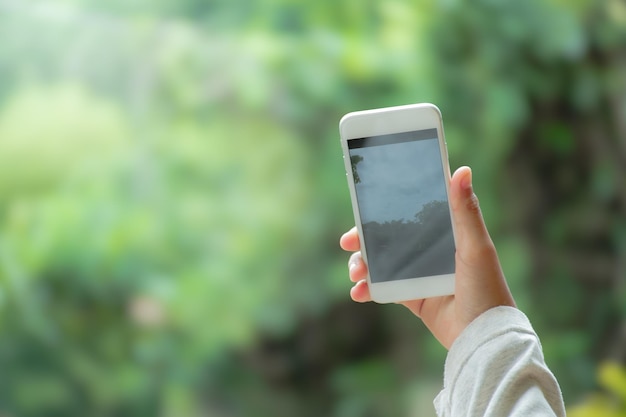 Photo hand holding a smartphone taking photos of forest and nature on mobile screen in camera mode in blurred natural background