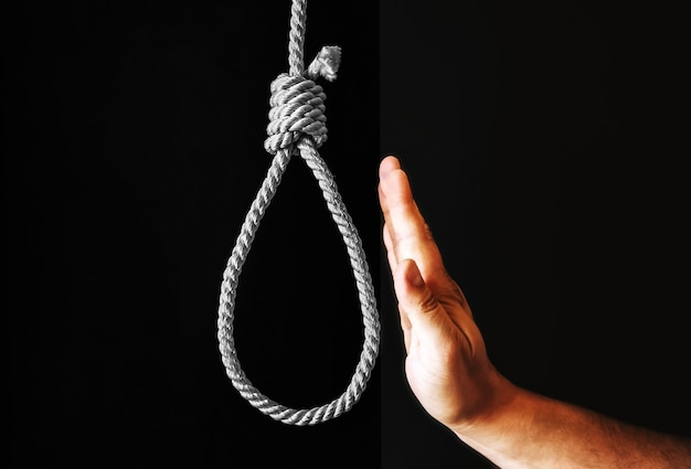 Photo hand near the noose on black background. stop suicide concept. hanging because of work stress. depression of burnout. terrible life situation.