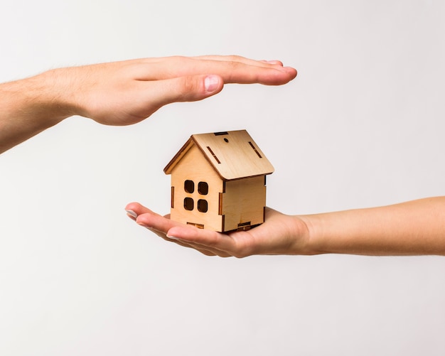 Hands protecting a wooden cottage