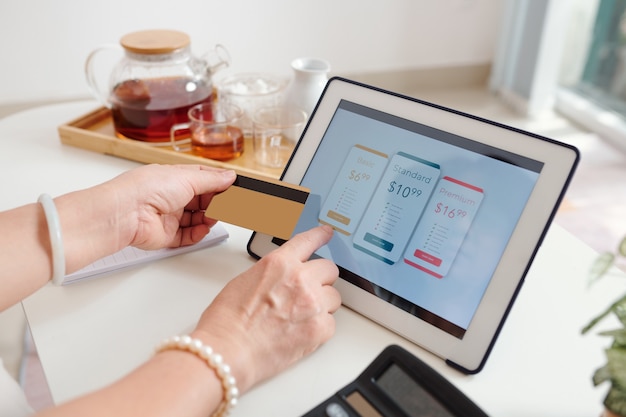 Hands of senior woman choosing subscription or payment plan on tablet computer and paying with credit card