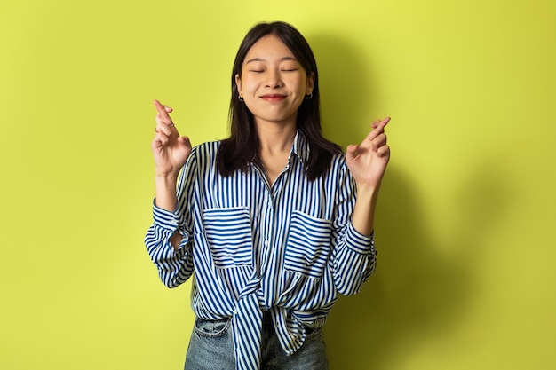 Photo happy asian woman crossing fingers for luck over yellow background