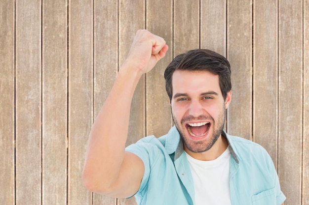 Happy casual man cheering at camera against wooden planks