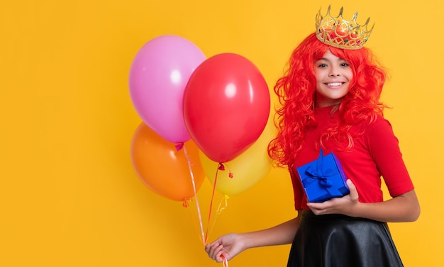 Happy child in crown with present and party balloon on yellow background