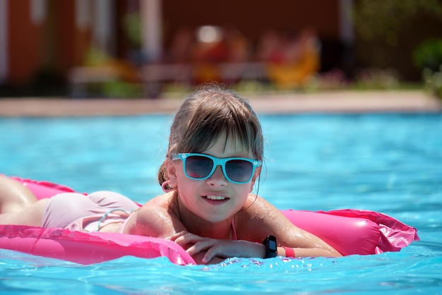 Happy child girl relaxing on inflatable air mattress in swimming pool on sunny summer day during tropical vacations Summertime activities concept