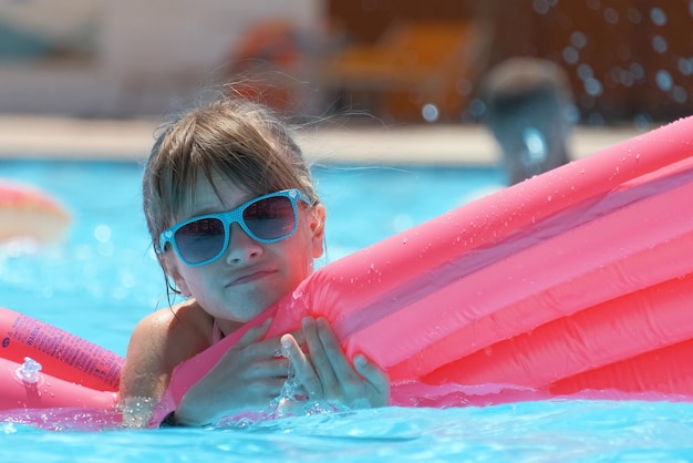 Happy child girl relaxing on inflatable air mattress in swimming pool on sunny summer day during tropical vacations Summertime activities concept