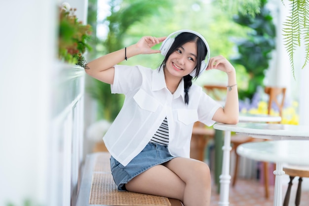 Photo happy of cute smiles asian of attractive young cute little girl wearing white wireless headphones and listening music enjoying favourite audio at the cafe on vacation at a coffee shop