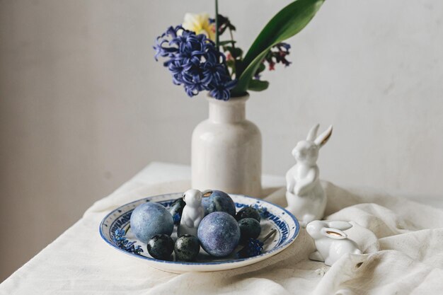 Photo happy easter stylish easter eggs on vintage plate bunny and spring flowers on linen napkin rustic table setting natural painted blue eggs and hyacinth blooms modern minimal still life