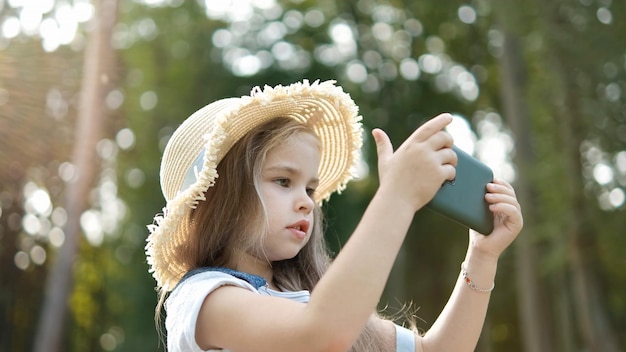 Happy smiling child girl looking in mobile phone outdoors in summer