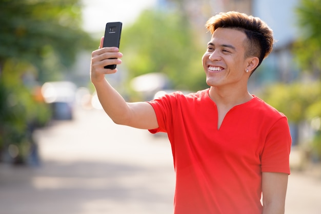 Happy young Asian man taking selfie in the streets outdoors