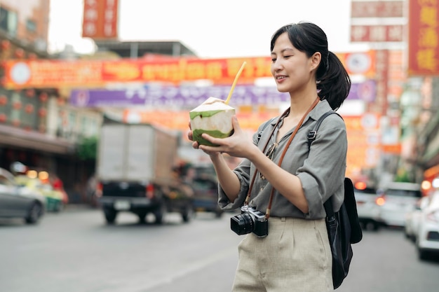 Photo happy young asian woman backpack traveler drinking a coconut juice at china town street food market in bangkok thailand traveler checking out side streets