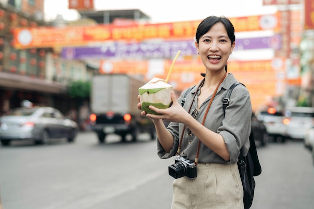 Photo happy young asian woman backpack traveler drinking a coconut juice at china town street food market in bangkok thailand traveler checking out side streets