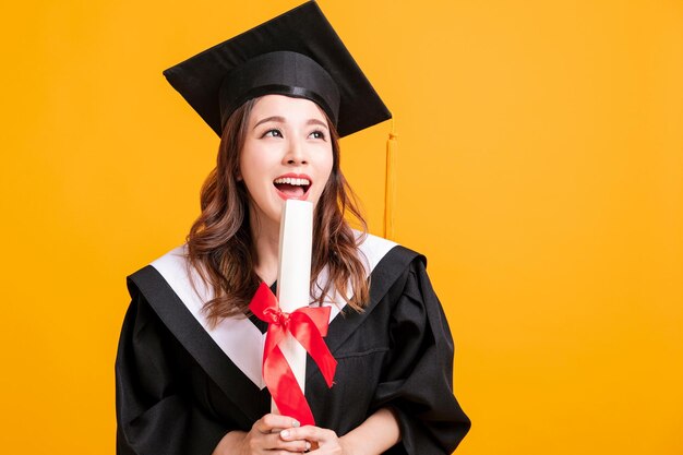 Photo happy young woman in graduation gowns holding diploma and looking away