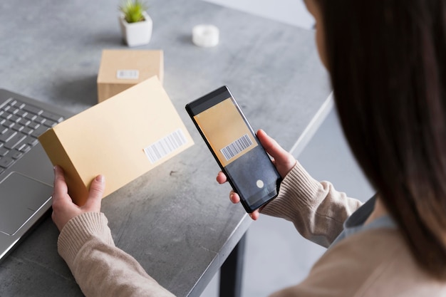 High angle of woman scanning bar code on box with smarphone