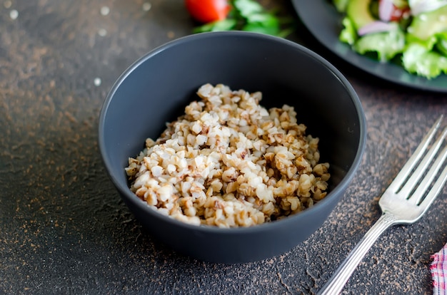 Foto porridge di grano saraceno caldo con burro fuso nella ciotola nera e insalata di verdure