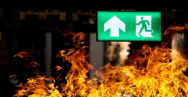 Photo hot flame fire and green fire escape sign hang on the ceiling in the warehouse at night the concept of fire escape training and preparation for evacuation