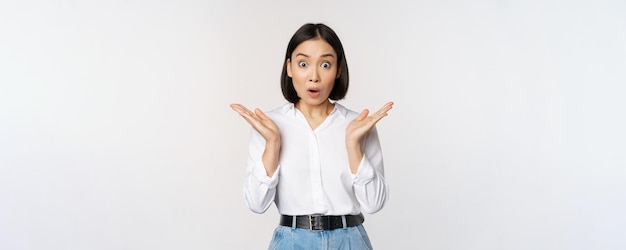 Image of asian female model looking surprised staring amazed reacting at surprise big news standing over white background