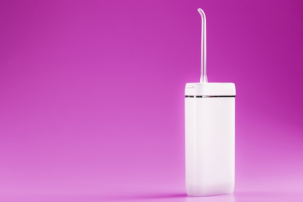 An irrigator for brushing teeth on a pink surface. Oral hygiene.