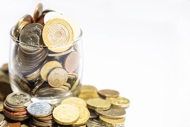 jar of money, various currency coins overflowing on white background