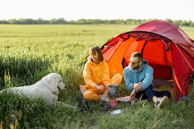 Jong stel gaat picknicken met een hond bij de tent op greenfield