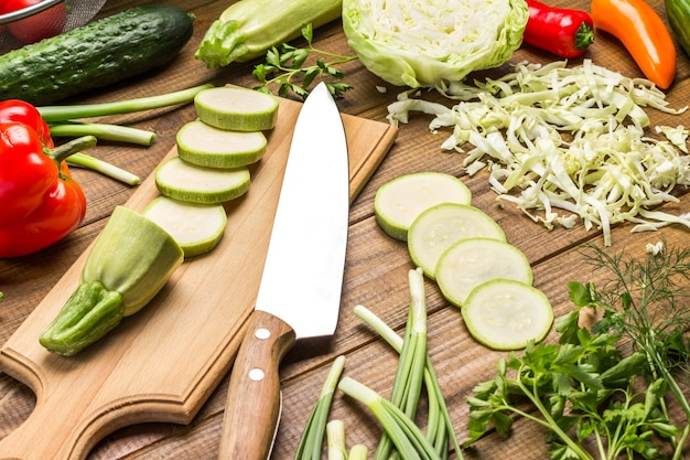 Kitchen knife and squash on cutting board. Sliced zucchini and cabbage on table. Wooden background. Top view