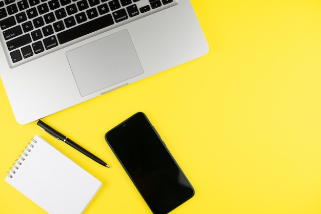 Laptop, pen, notepad planner and smartphone on yellow background.