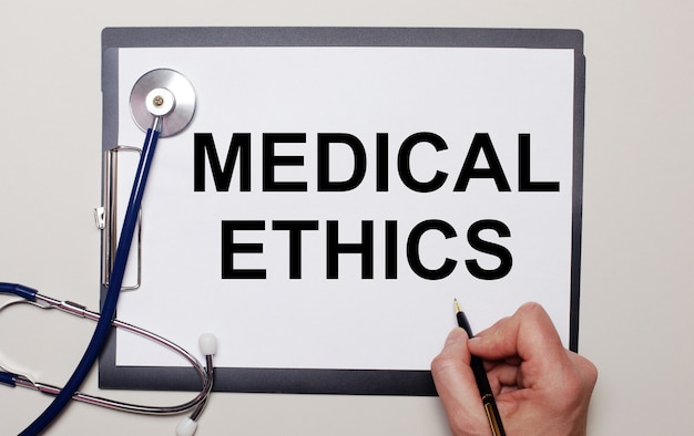 On a light surface, a stethoscope and a sheet of paper, on which a man writes MEDICAL ETHICS