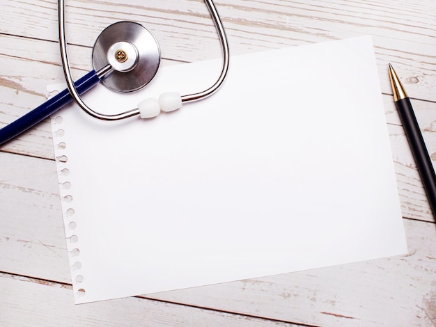 On a light wooden table there is a stethoscope, a pen and a sheet of paper with a place to insert text. Medical concept