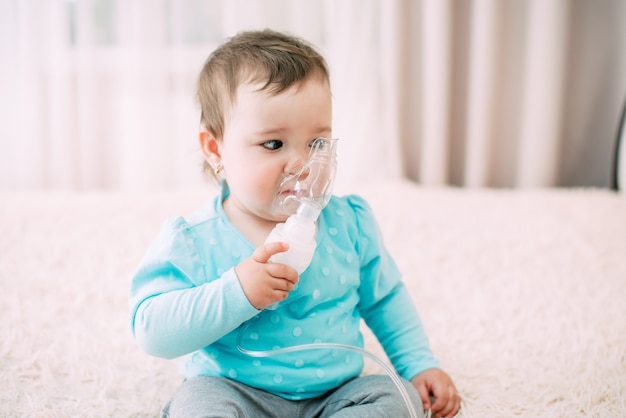 A little girl yourself holding the mask of the nebulizer, making inhalation very sweet