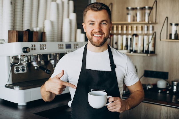 Male barista at coffee shop holding cup by the counter