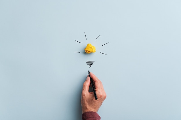 Photo male hand drawing a light bulb over blue background in a conceptual image.