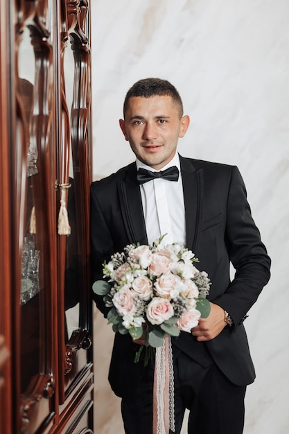 Photo a man in a black suit and bow tie holding a bouquet of flowers