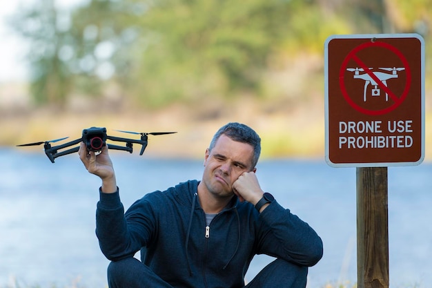 Man is sad that he is not allowed to fly his quadcopter state park no drone area Operator is unauthorised to use UAS near restriction sign