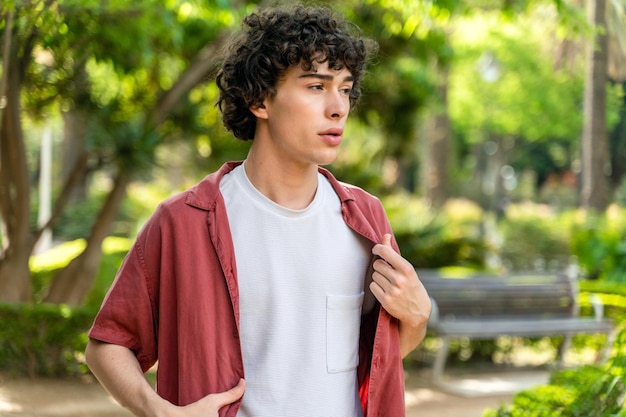 Foto man met krullend haar in een casual shirt die wegkijkt tijdens het wandelen op een zonnige dag