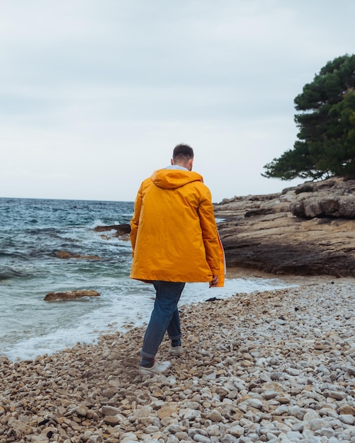 Man walking by rocky beach in yellow raincoat overcast windy weather