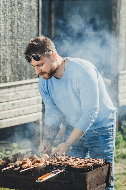 A man with a beard near the fire and the grill fry meat and sausages