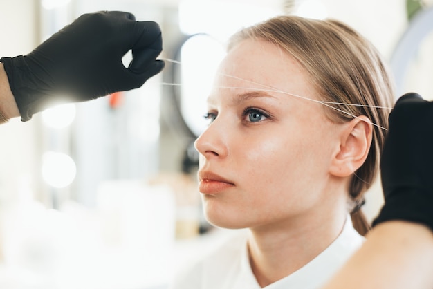 Master brow artist corrects eyebrows using a thread in the salon effectively