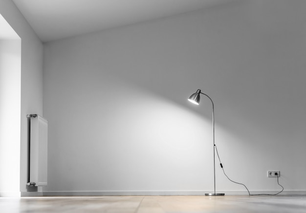 Metal floor lamp in empty room with shadow on white wall, copy space for text