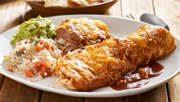 Mexican burrito platter with red enchilada sauce, fried beans, rice and guacamole