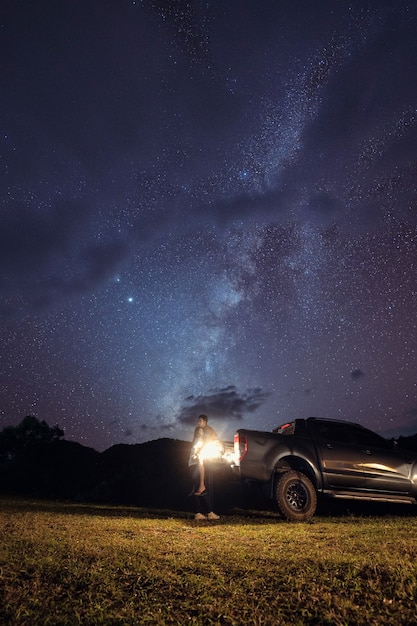 Milky way over mountain and young couple embracing on pickup at night