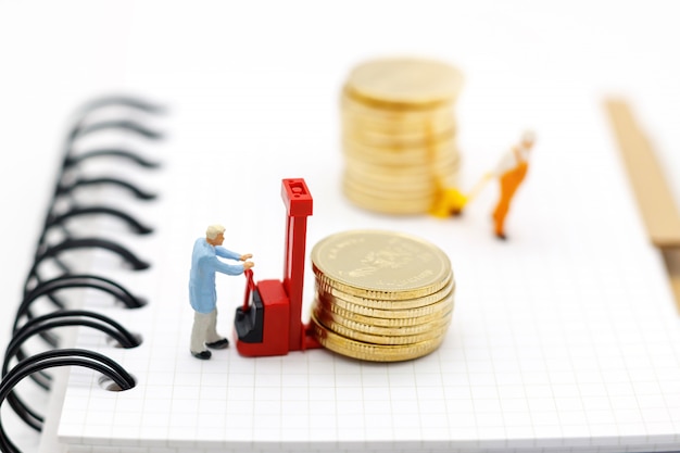 Miniature people: workers transport coins money on book.