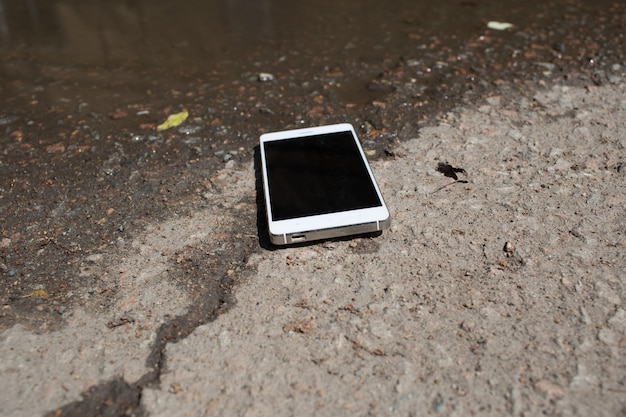 Mobile phone lying on pavement in puddle.