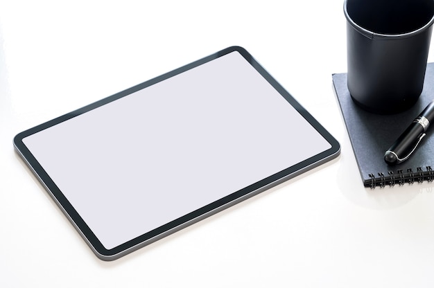 Photo mockup blank screen tablet with black paper cup, pen and notebook on white table, top view.