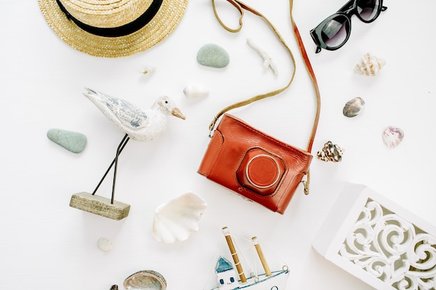 Photo modern composition with bird figurine, toy boat, retro camera, sunglasses, seashells and straw hat on white surface