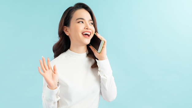 Photo modern lifestyle and communication smiling beautiful girl talking on phone while standing on blue background