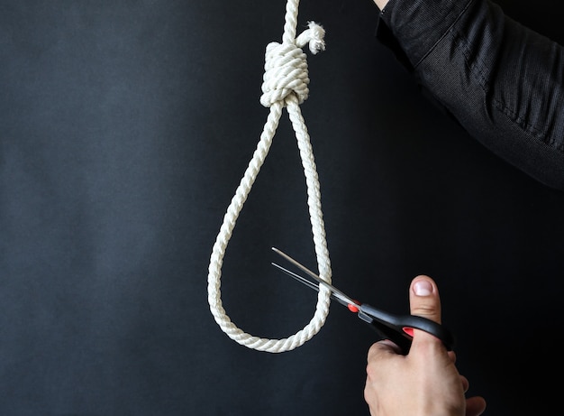 Photo noose on the neck. man holding scissors in hands. suicide concept. hanging because of work stress. depression or burnout. terrible life situation. life choice.