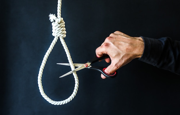 Photo noose on the neck. man holding scissors in hands. suicide concept. hanging because of work stress. depression or burnout. terrible life situation.