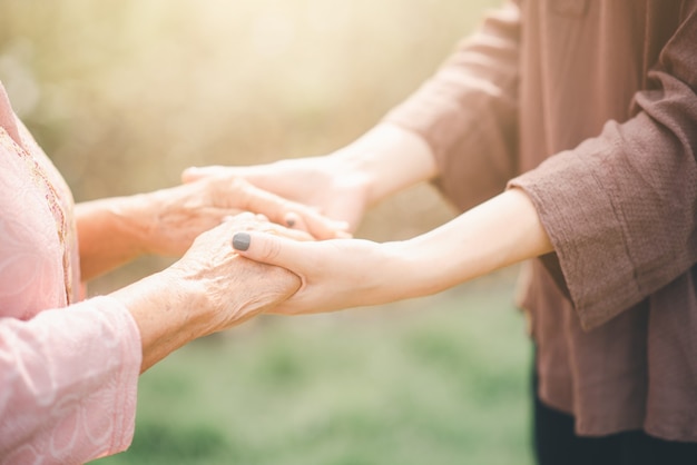 Foto oude en jonge vrouw hand in hand elkaar zorvuldig in zonlicht