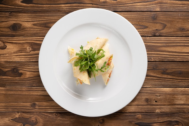 Photo pancakes stuffed with salmon, cream cheese, lettuce and arugula in a white ceramic plate on a wooden kitchen table.