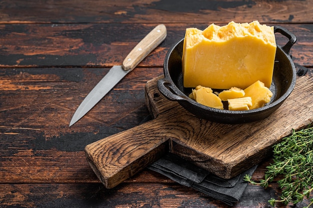 Photo parmesan hard cheese piece in a pan. dark wooden background. top view. copy space.